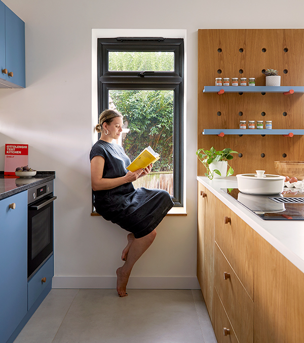 Woman sits nicely while reading on a window seat by the Kitchen area.