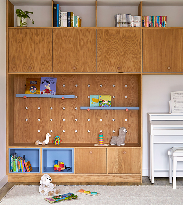 Kids playing area organised by a bespoke joinery with a seating area, open blue niches, wooden boxes and adjustable blue shelves supported by red supports for books.